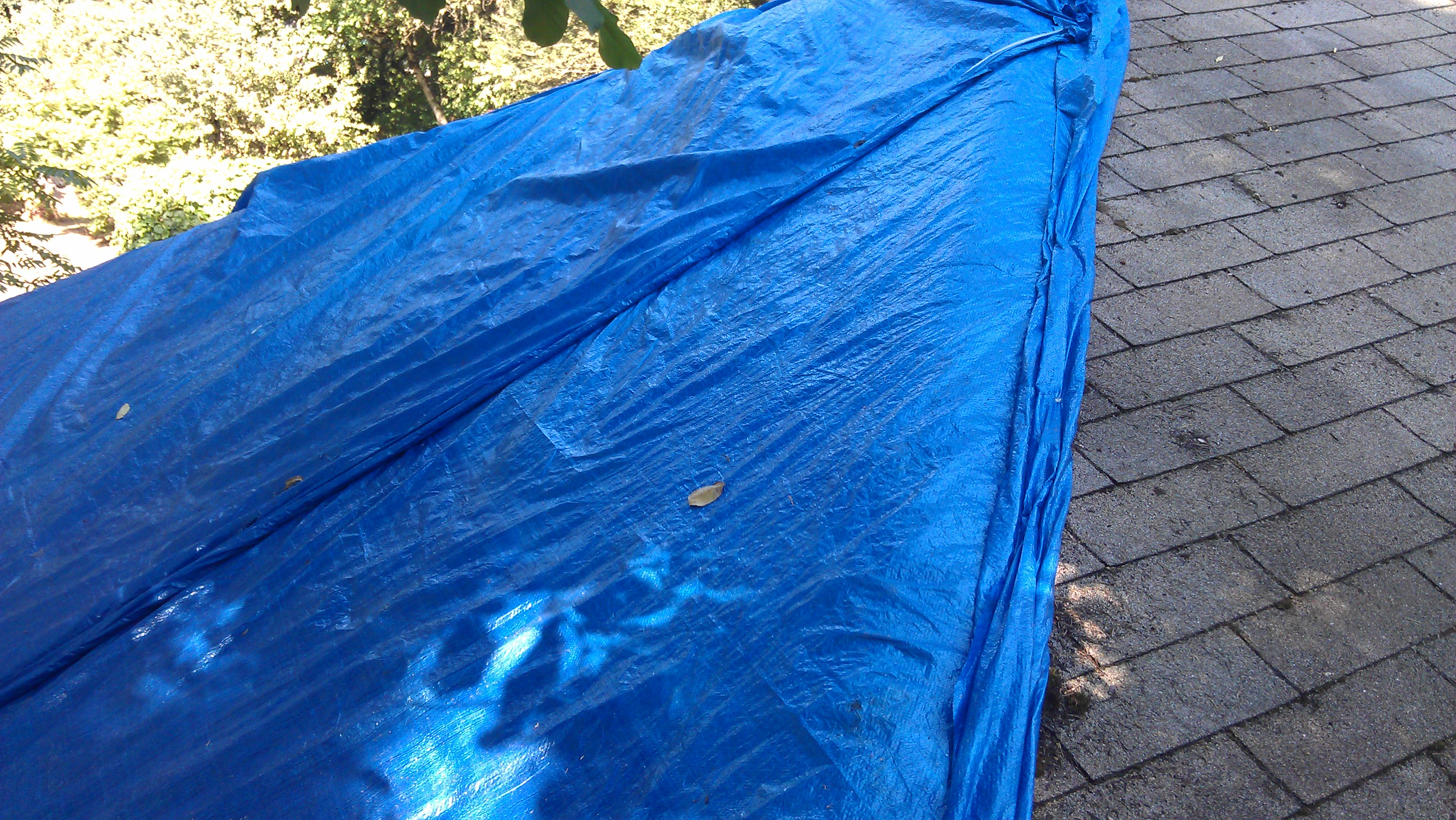 Blue tarp sealed tight over a Portland roof ridge for a temporary emergency leak fix