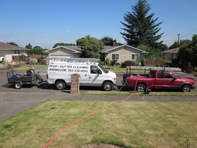 The JNR van and trailer set up in a driveway with a hose run to the house for a roof cleaning job